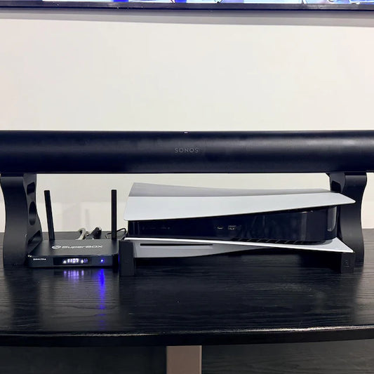 Sonos Arc Ultra on two tall black riser supports, with a PS5 and network device underneath on a media shelf.