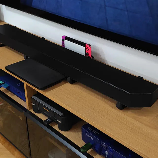 Black soundbar on a wooden entertainment console with electronic devices.